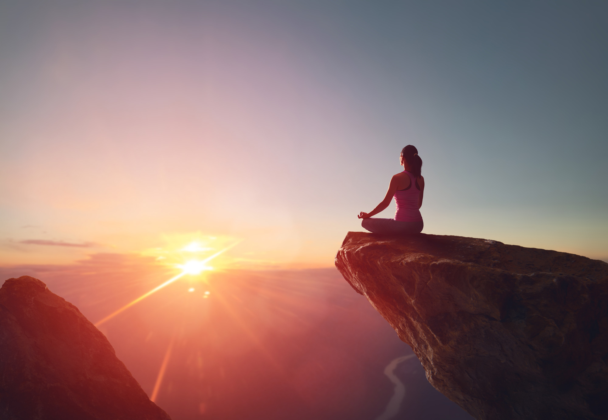 Woman meditating on rock at sunrise